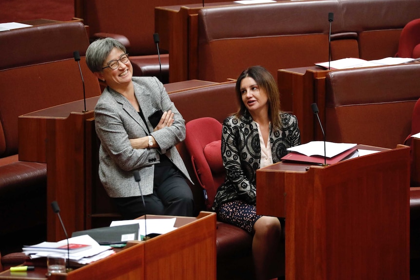 Senator Wong is laughing with arms folded as she talks to Senator Lambie, who is sitting on the crossbench.