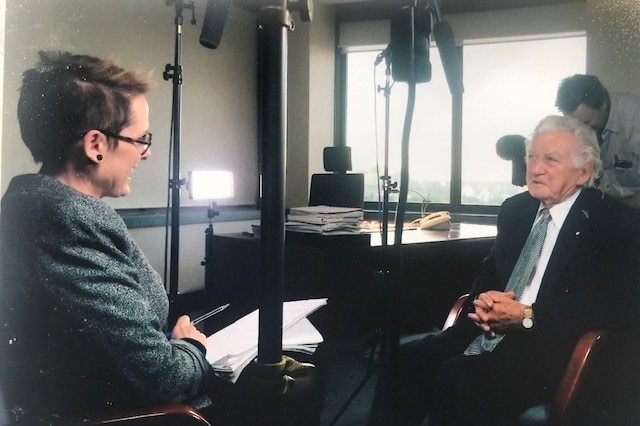 Woman interviewing a man with cameraman and sound equipment around them.