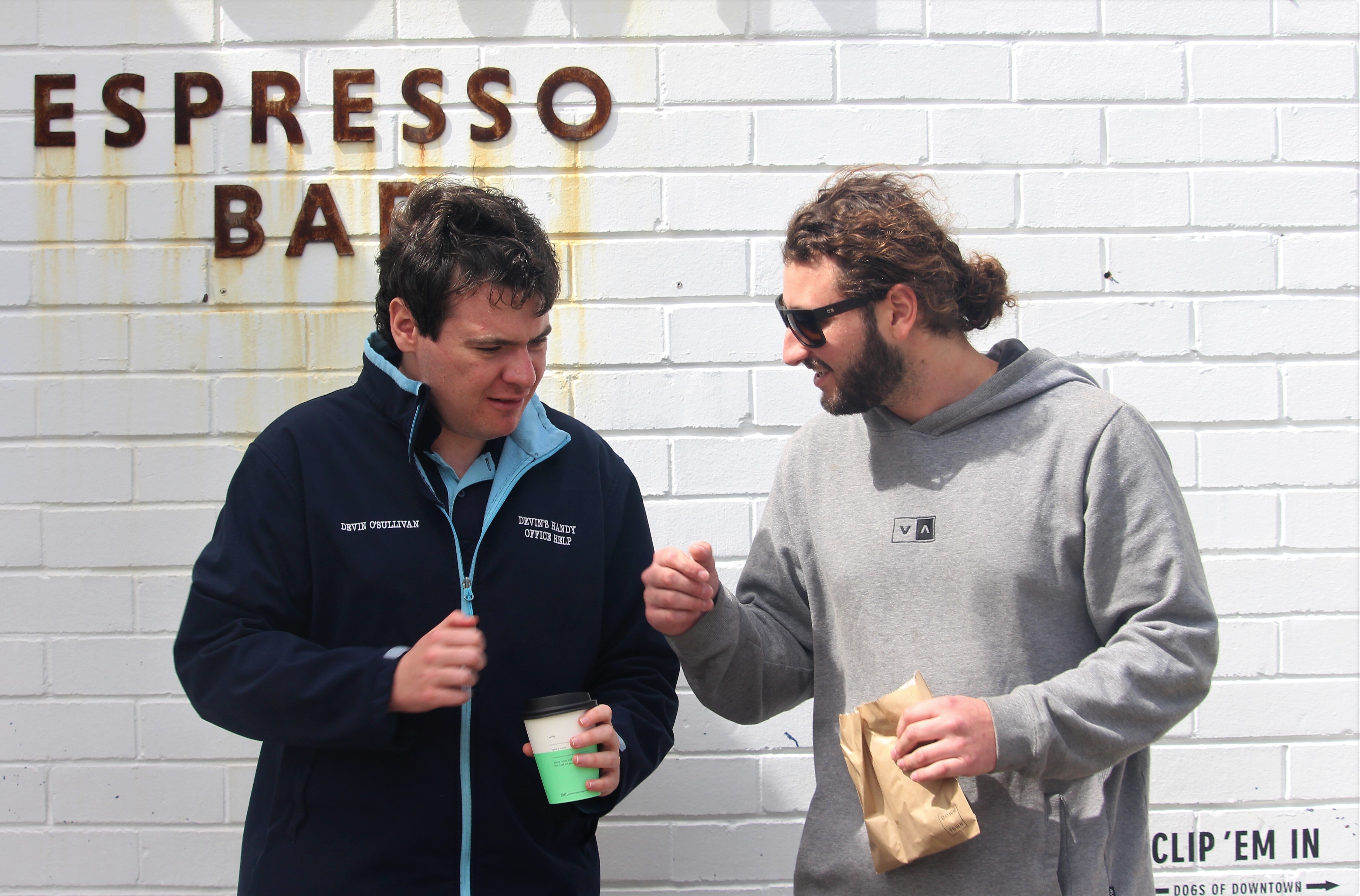 young business owner wearing a uniform fist bumps his support worker in front of a cafe