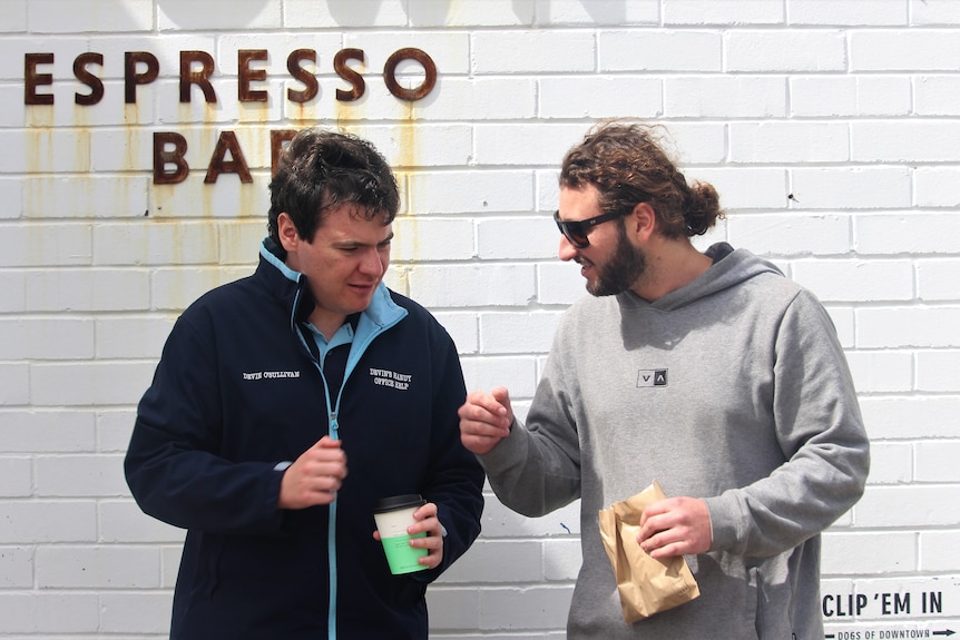 young business owner wearing a uniform fist bumps his support worker in front of a cafe