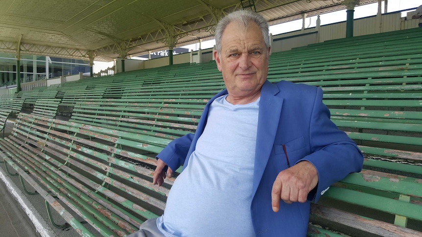 Greg Rider sits on a seat at a racetrack.