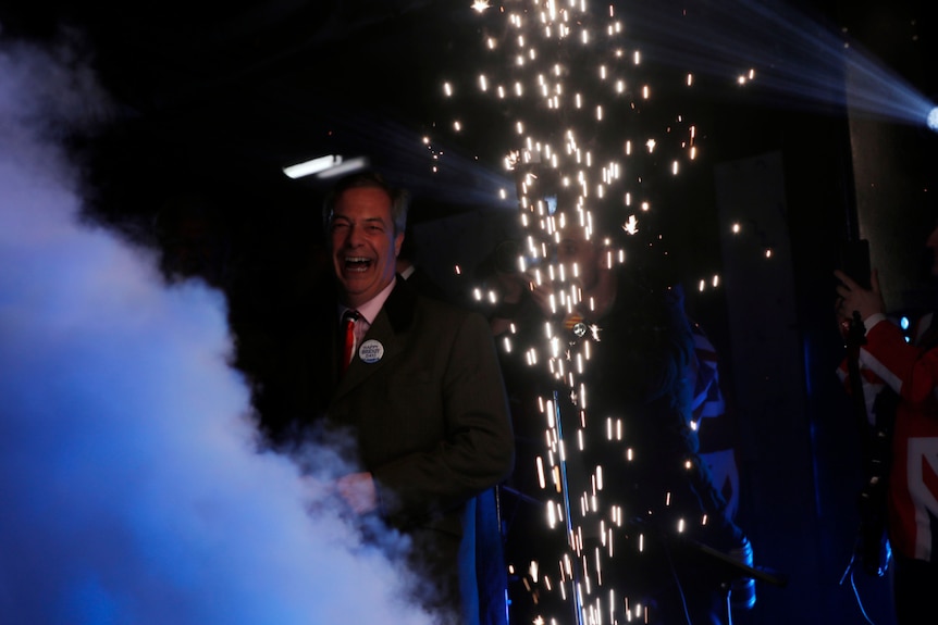 Nigel Farage smiles as smoke and fireworks rise in the dark