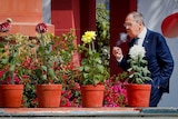 Sergei Lavrov standing behind a row of potted flowers smoking a cigarette
