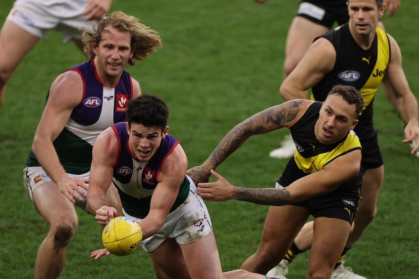 A Dockers player releases a handball under pressure as a Richmond player tries to grab him.