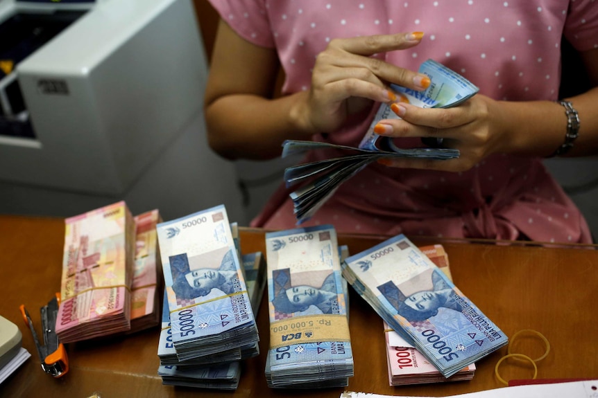 A teller counts Indonesian rupiah at a money changer