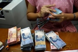A teller counts Indonesian rupiah at a money changer