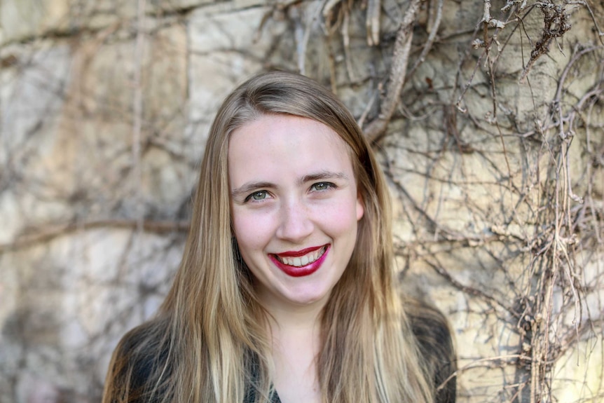 A young woman with long blonde hair and red lipstick smiles in a photo portrait