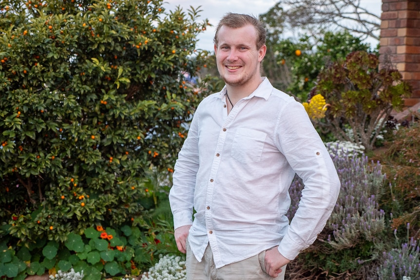 A young man stands in the garden in front of their family home.