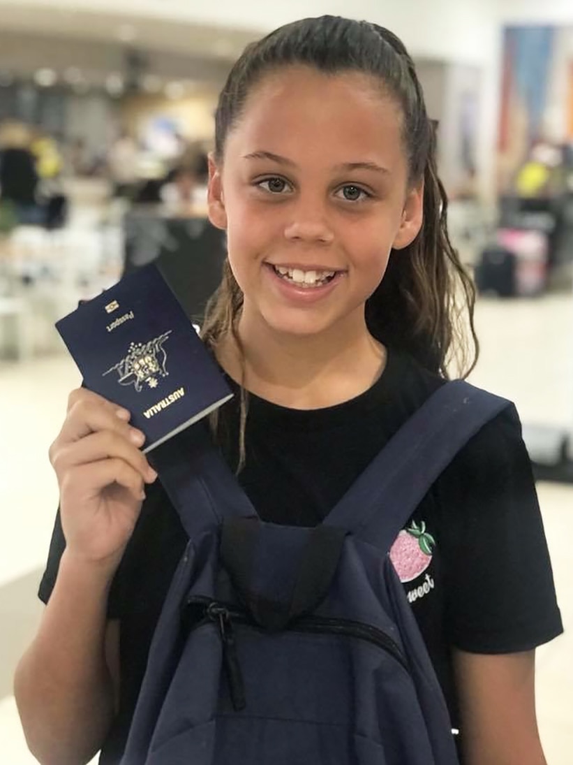 A young girl holds up her Australian passport