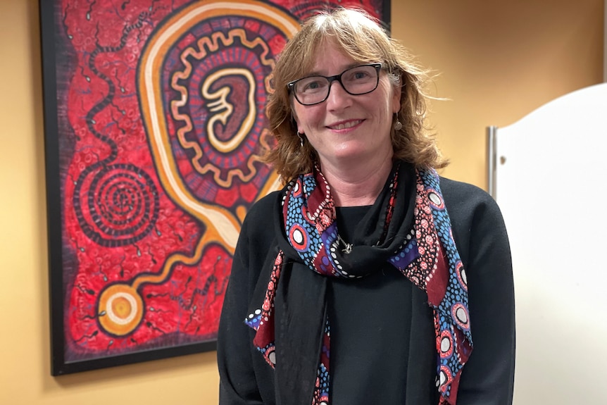 A woman in glasses and spectacles in front of an Aboriginal art painting