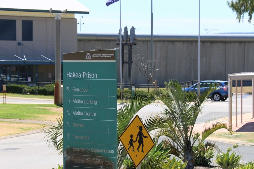 Blue sign shows entrance to prison.  Prison building is in the background.