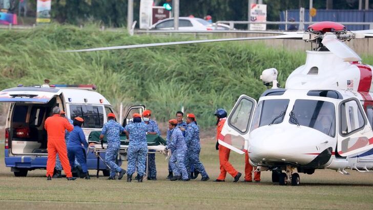 Officials in blue camouflage print transport a body on a stretcher from a helicopter to a van.