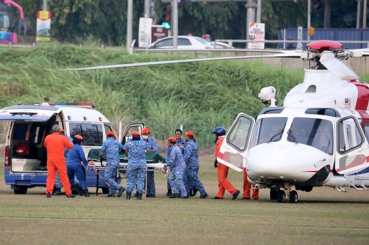 Officials in blue camouflage print transport a body on a stretcher from a helicopter to a van.