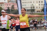 A marathon runner jogs on the pavement with her arms spread wide like a bird.