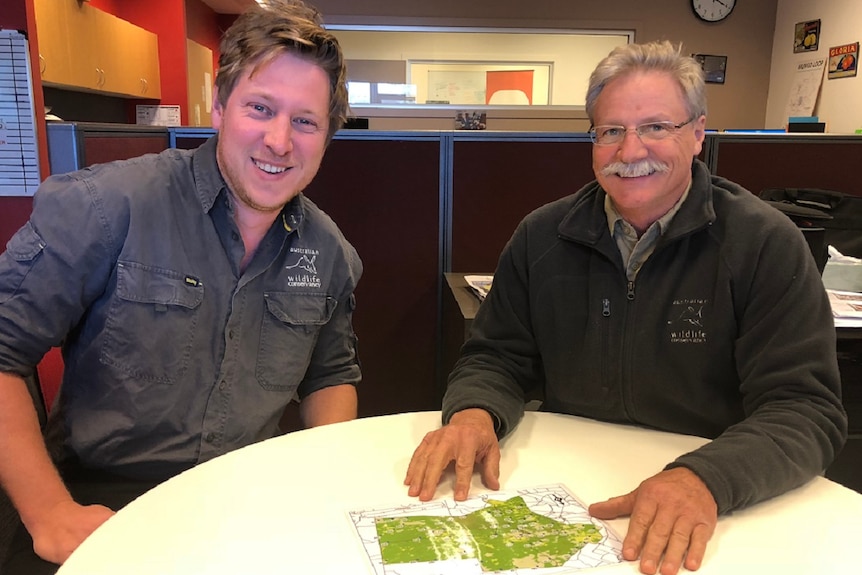 Two men, one younger, one older sitting at a table, looking at maps