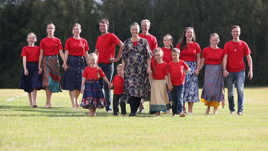 A family of 14 walk hand-in-hand while wearing matching red shirts.