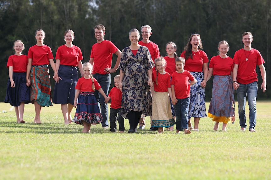 A family of 14 walk hand-in-hand while wearing matching red shirts.