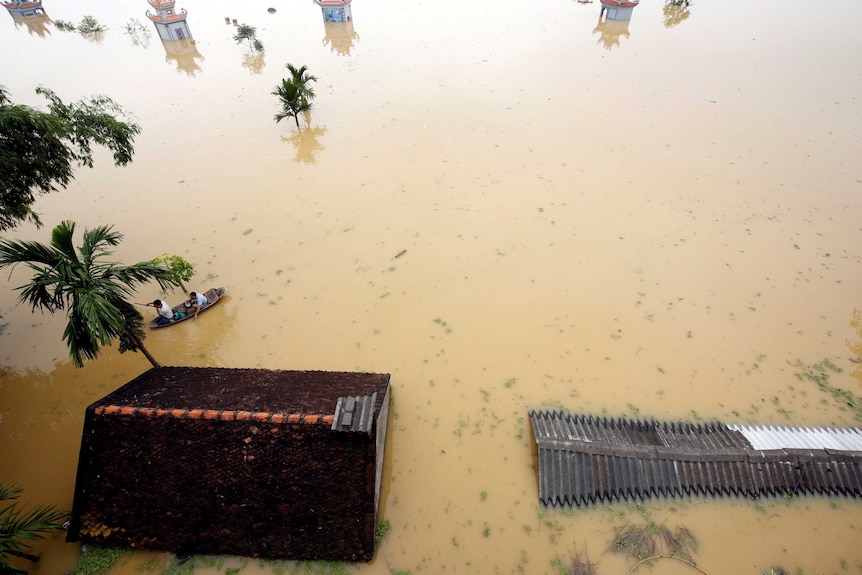 Farmers paddle in a boat through a flooded village.