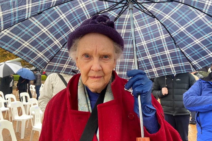 An older woman, holding an umbrella and looking serious.