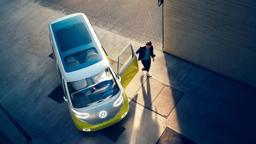 A man walks away from a small modern van, with its bright headlights and Volkswagen logo illuminated.