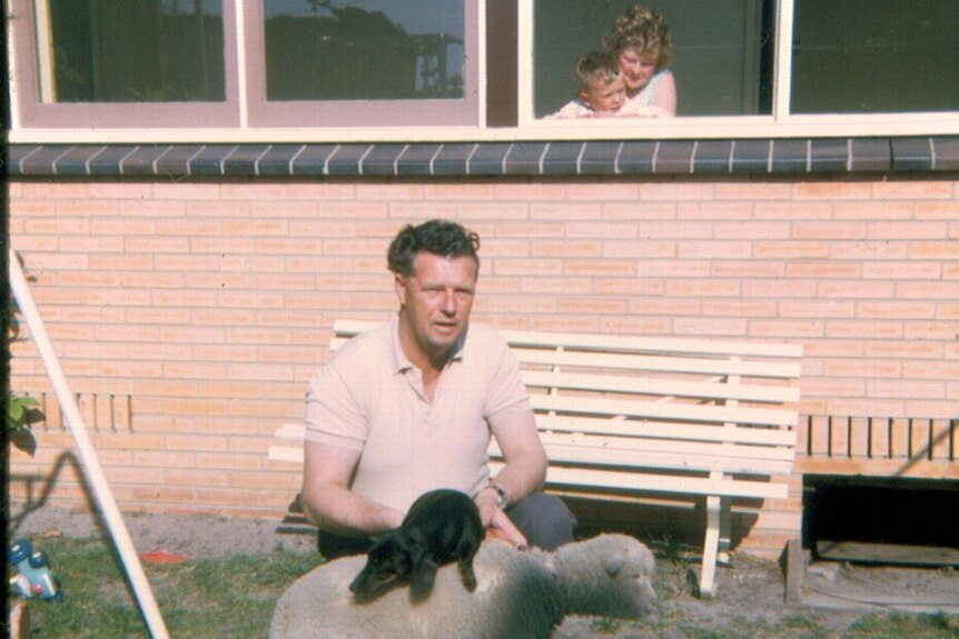 An old photo of Peter as a baby being held by his mum, while his dad outside squats next to a sheep