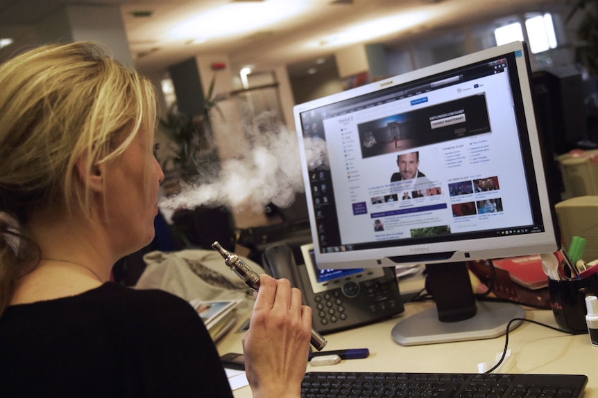 A woman smokes an e-cigarette in an office environment