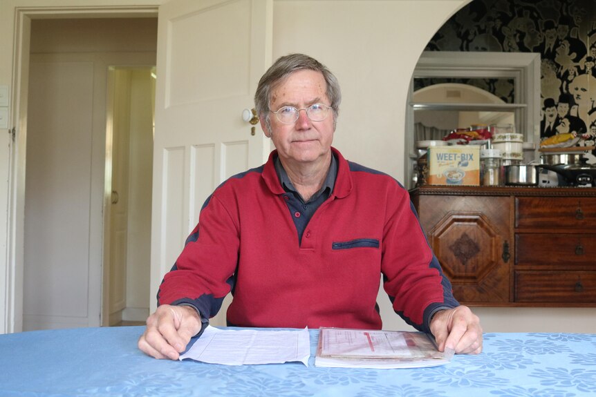 A man wearing glasses sits at a table with papers.