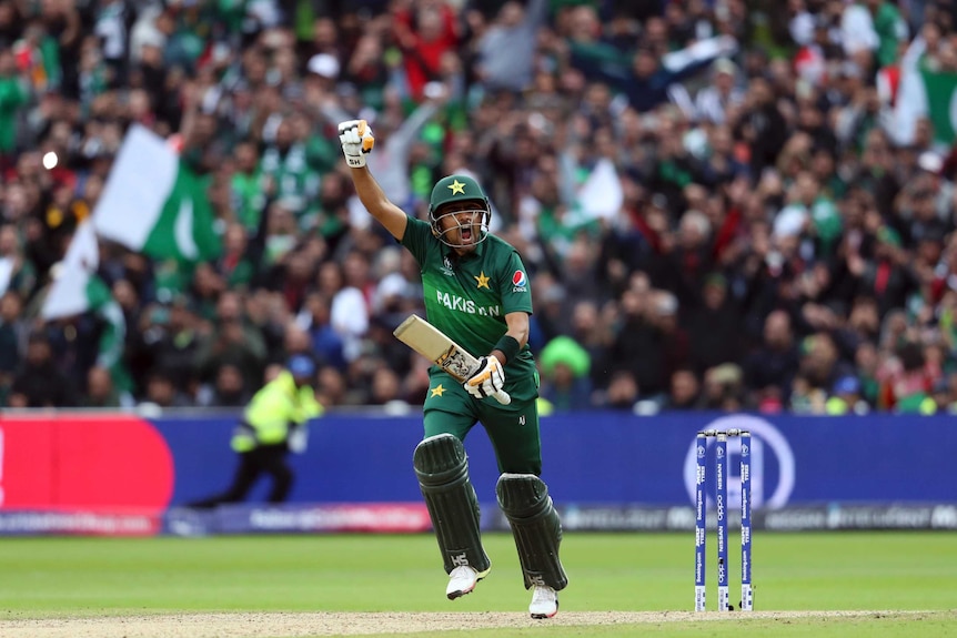 A batsman raises a gloved fist in the air as he runs down the pitch after scoring a century.