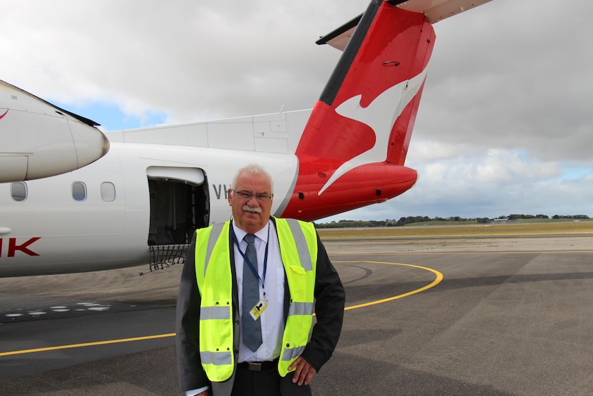 Un homme en costume et gilet haute visibilité se tient devant l'arrière d'un petit avion