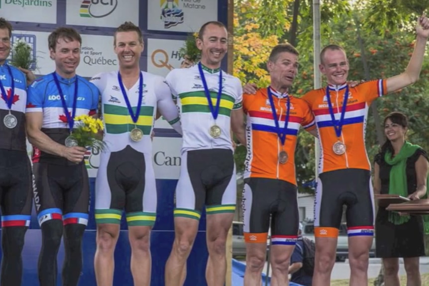 Six men on a stage in cycling uniforms with medals around their necks.