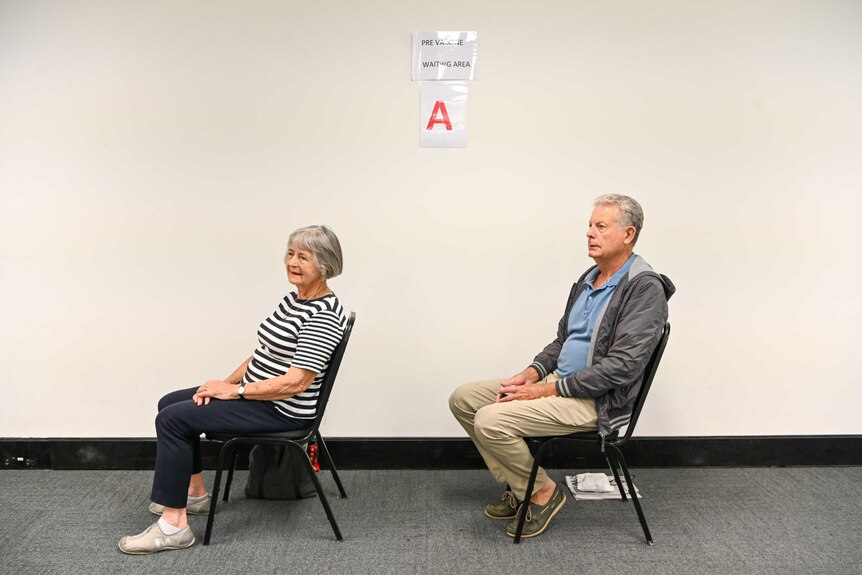 A man and a woman sit on chairs 1.5m apart in a vaccination waiting room.