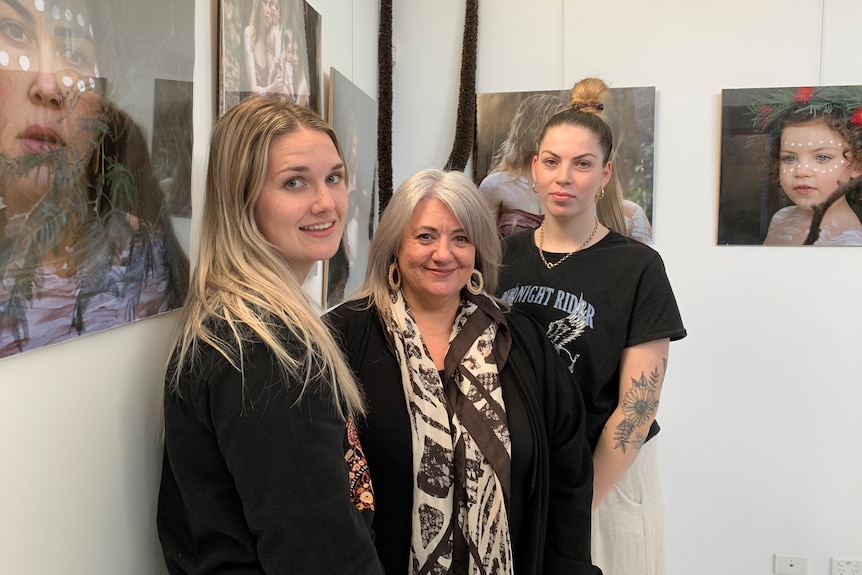 Brittany Wright, Tania Martini and Mahlia McDonald in front of photographs of children and mothers hanging in a gallery