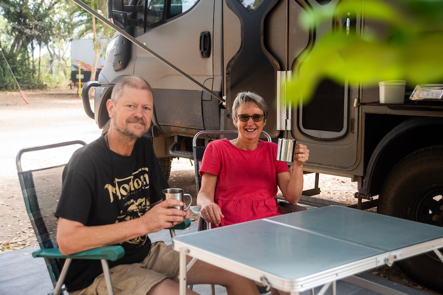 A man and a woman sit at an outdoor fold-up table drinking coffee.