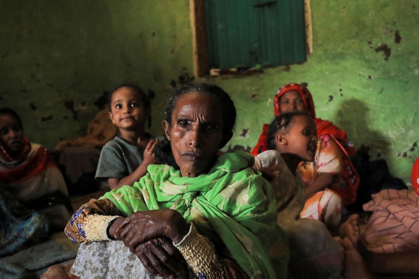 A displaced woman from the Amhara region sits in a camp looking at the camera with children behind her. 