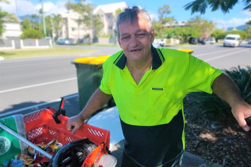 A man in a yellow shirt stands near some bins.