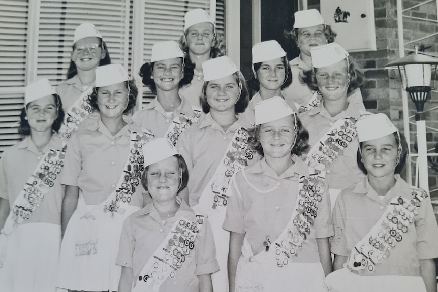 Foto hitam putih gadis-gadis yang mengenakan rok, kemeja, dan topi putih