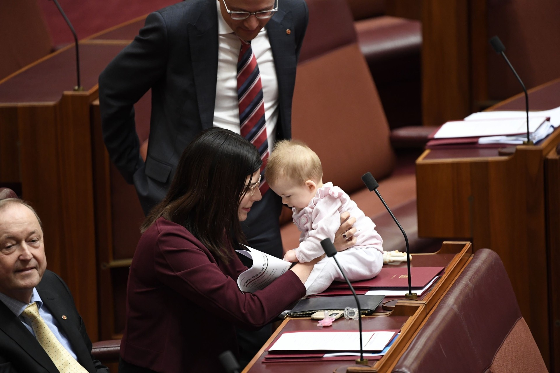 A woman holds her baby who is sitting on a desk inside the Senate