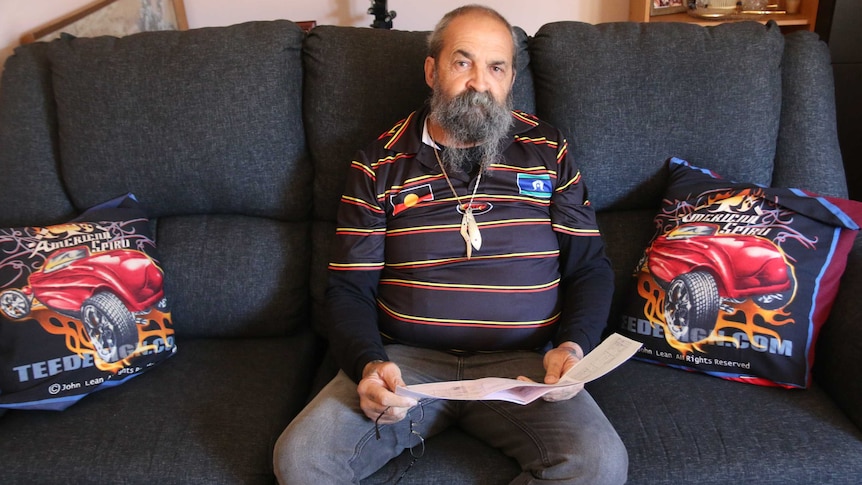 Garry Smith sits on his lounge, holding documents which he claims have whitewashed his family history.