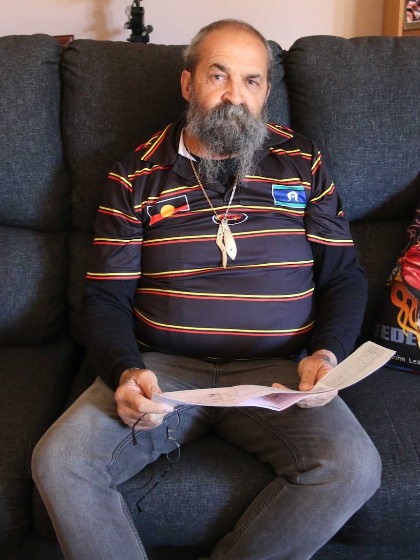 Garry Smith sits on his lounge, holding documents which he claims have whitewashed his family history.