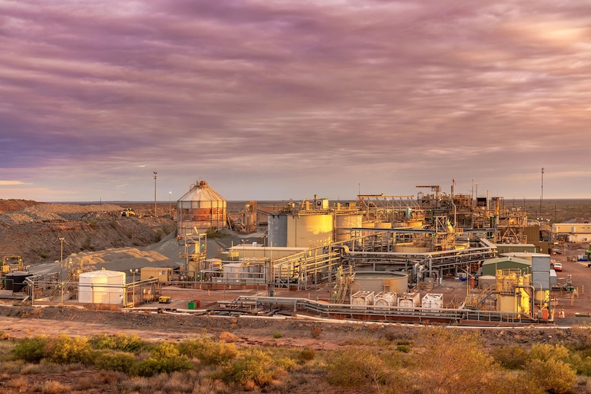 A wide shot shows facilities at a gold mine, as the sun sets and turns the sky purple