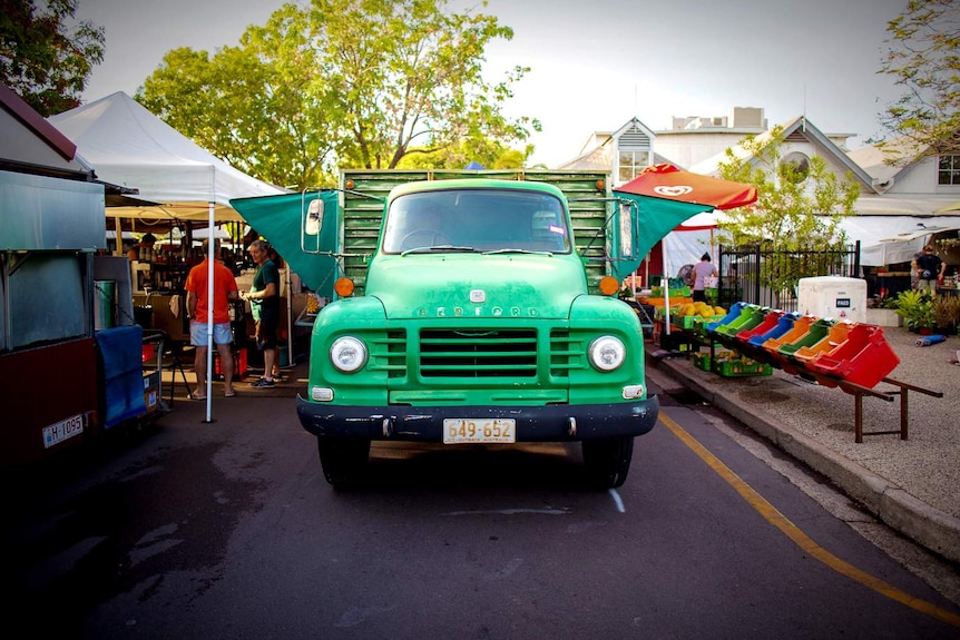 A 4:3 of an elderly green truck shot head-on with awnings and fruit and veg crates laid out