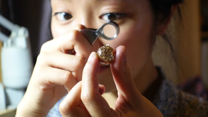 Mana Ohori looks at a piece of jewellery through a magnifying glass.