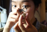 Mana Ohori looks at a piece of jewellery through a magnifying glass.