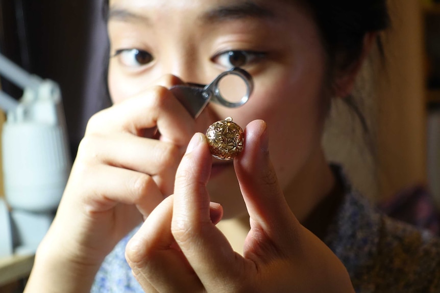 Mana Ohori looks at a piece of jewellery through a magnifying glass.