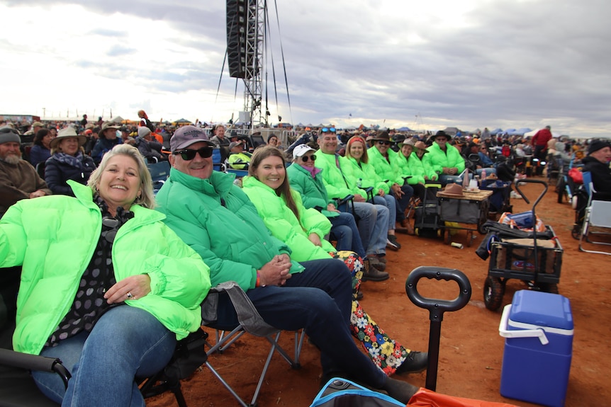 a row of smiling people sitting in a crowd wearing bright green jackets