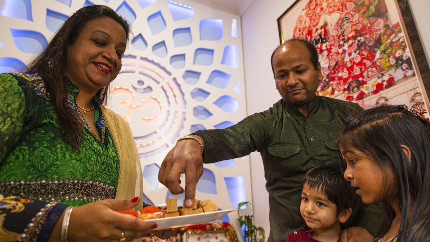 A man reaches into a plate of food as a woman and children look on happily.