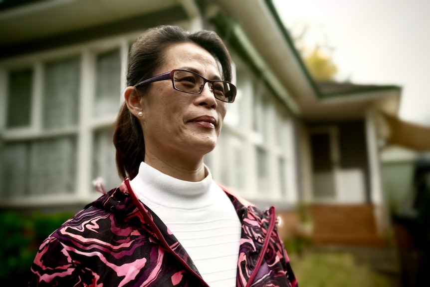 A middle-aged woman wearing sunglasses and her in hair in a ponytail looks off into the distance.