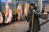 A man in a coat smiling next to a row of animal carcasses hanging