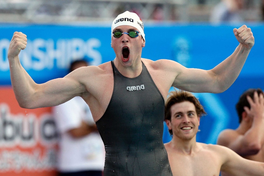 Paul Biedermann wears a black swimming suit that covers his torso and clenches his fists with his mouth open