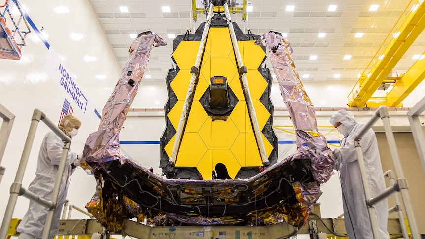 Workers in white suits work on the James Webb Space Telescope